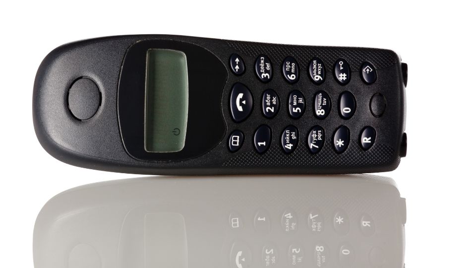 Ein schwarzes DECT-Telefon mit Tasten und Display auf einem reflektierenden Tisch.