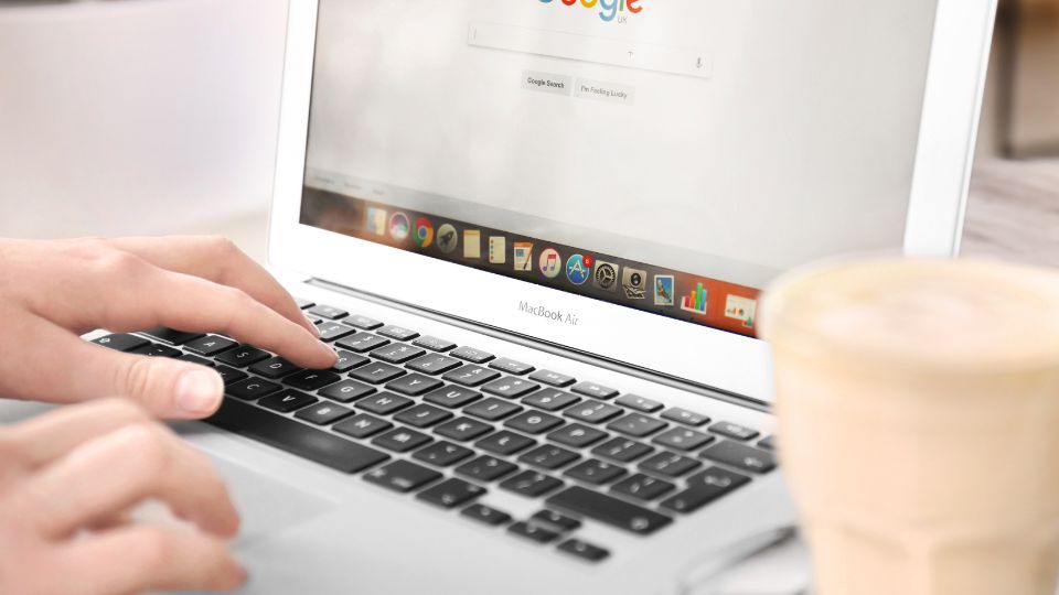 Eine Hand tippt auf der Tastatur eines MacBook Air, während Google geöffnet ist.